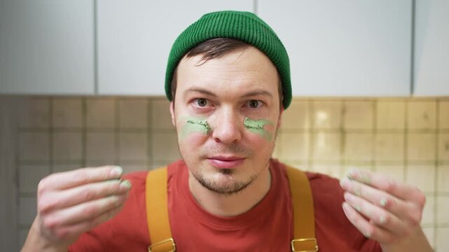 Playful construction worker in a beanie comically applying green tile grout under his eyes, mimicking eye black like a football player, before starting a home improvement job