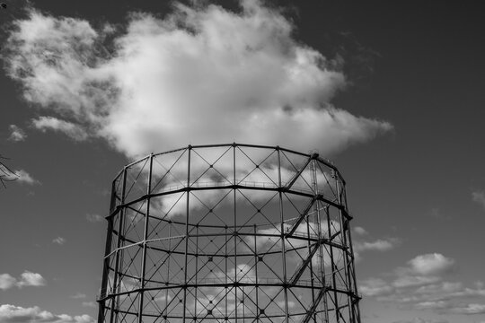 Gasometer industrial structure in urban architecture rendered monochrome with steel framework under sky clouds leaving space for copy text