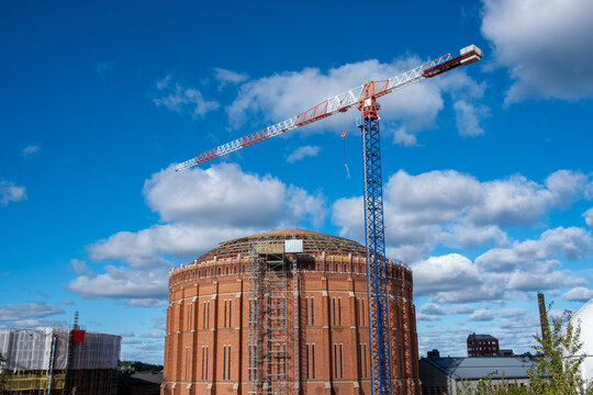 Crane construction above gasometer industrial architecture in urban area with daylight sky clouds and open space for copy on clean background
