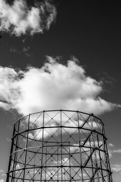Gasometer industrial structure in monochrome showing steel architecture in urban skyline with sky clouds and negative space for copy