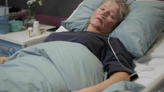 Tilt up shot of mature Caucasian female patient with nasal cannula resting in hospital bed while receiving oxygen treatment in modern comfortable ward