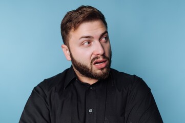 Obraz premium Surprised man reacts to unexpected news while standing against a blue backdrop