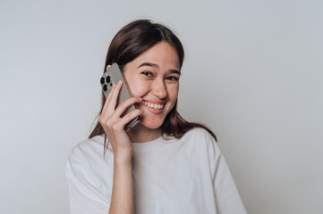 Fototapeta premium Smiling young woman enjoys a joyful conversation on her smartphone in a bright, minimalist setting