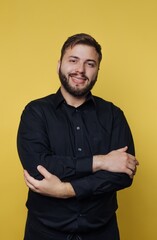 Fototapeta premium Young man with a friendly smile poses confidently against a bright yellow background while wearing a stylish black shirt