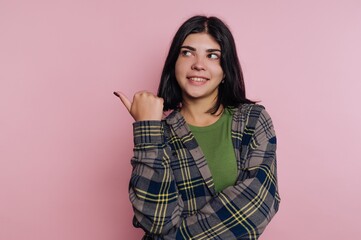 Fototapeta premium Smiling young woman in a casual flannel shirt gestures playfully against a soft pink background