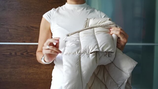 Headless view of young woman putting on vest in front of wardrobe. Everyday clothing routine, getting dressed process and lifestyle moment at home.