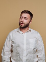 Obraz premium Young man with a beard in a white shirt gazes thoughtfully against a warm beige background