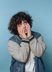 Child with curly hair displaying a dramatic expression against a blue background in a playful moment of surprise or contemplation