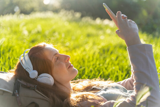 Young redheaded woman with headphones and smartphone in a park