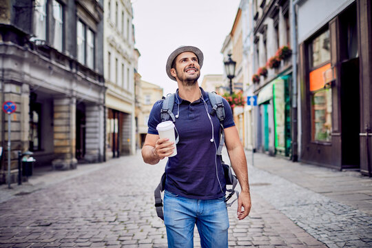 Traveler with backpack walking down city street and holding coffe