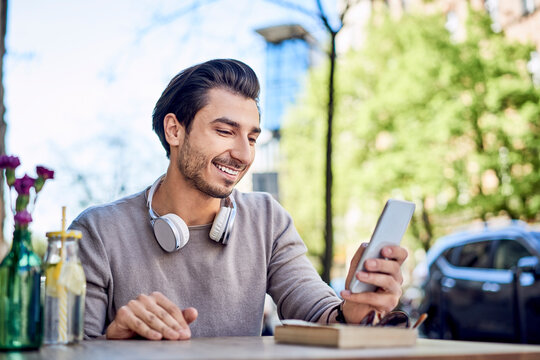Happy young man using cell phone at outdoors cafe