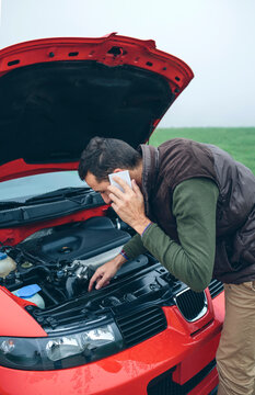 Man on cell phone looking at broken engine car