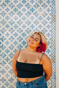 Young woman standing with hand behind back against wall