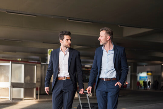 Two businessmen with rolling suitcase at bus terminal