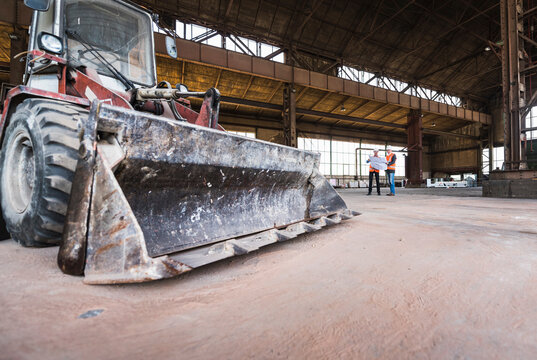 Two men with plan wearing safety vests talking in old industrial hall