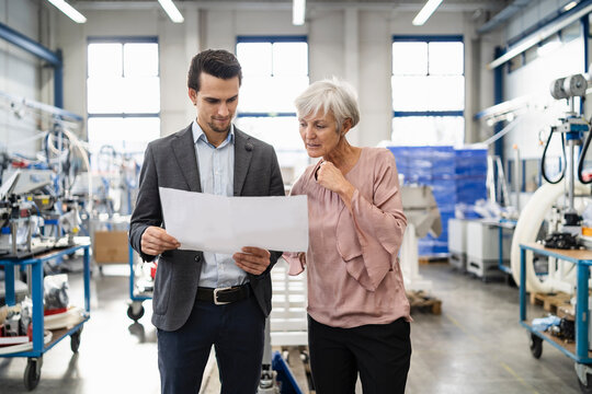 Businessman and senior woman looking at plan in a factory