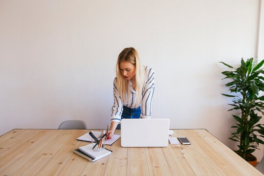 Young businesswoman standing at desk, using laptop