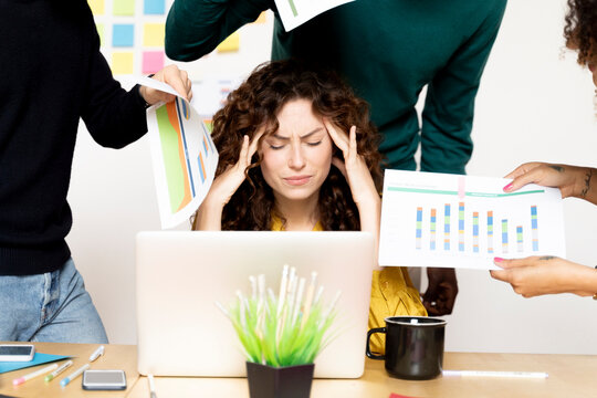 Stressed woman siting at desk in office surrounded by colleagues