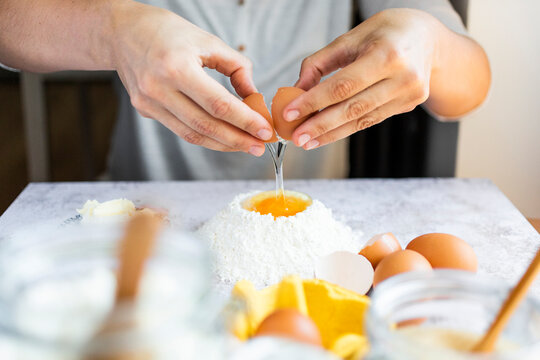 Hands of woman breaking egg into flour heap