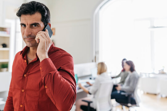 Businessman talking on the phone in office with colleagues working in background