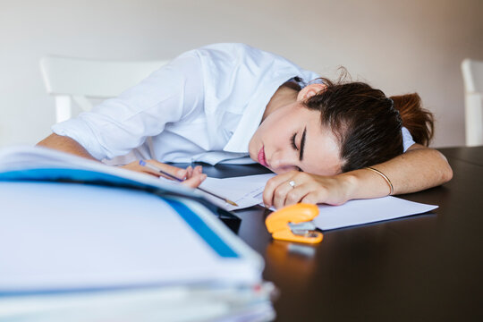Exhausted female student lying on desk at home with documents