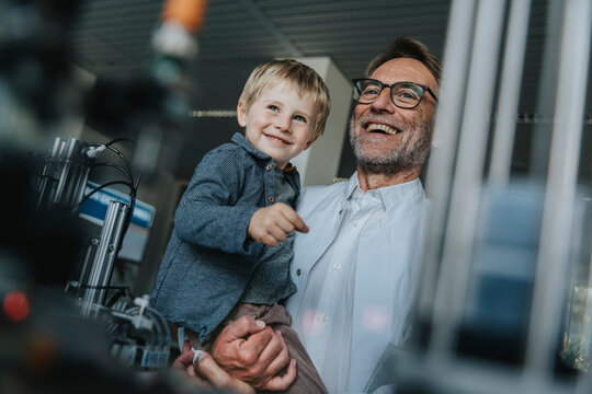 Happy scientist father carrying son while standing in laboratory at factory