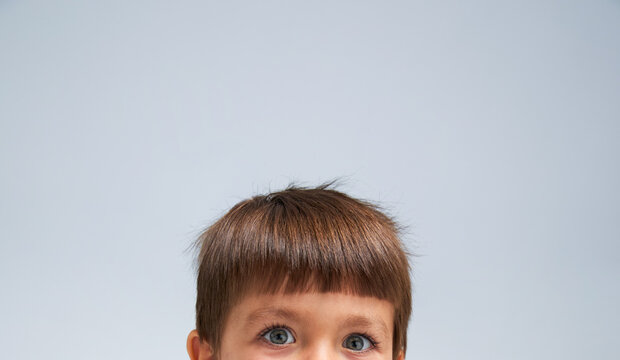 Close up image of a 5 year old little boy, looking at camera. Grey background.