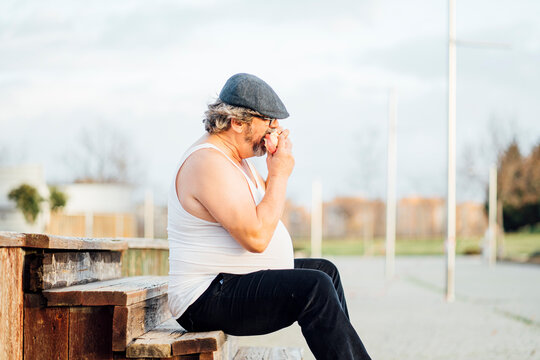 Man with beer belly sitting on steps and eating a sandwich