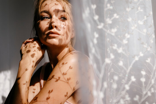 Shadow of curtain on seductive woman sitting at home