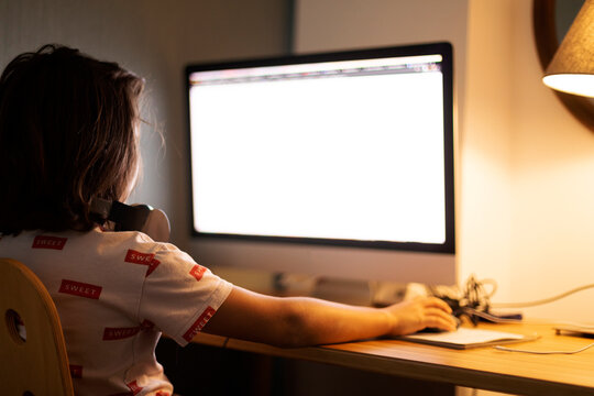 Rear view of boy using computer while sitting at illuminated desk