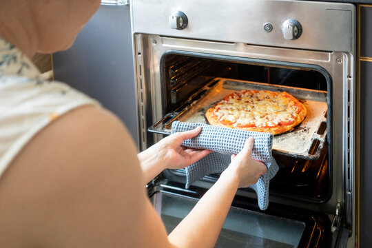 Crop view of woman taking tray with baked pizza out of oven