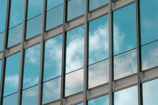 Glass facade windows with modern architecture grid and reflection capturing clouds and sky creating an abstract pattern backdrop for business use