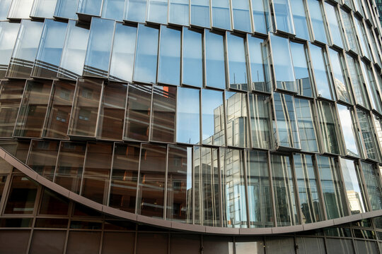 Abstract modern building facade with curved glass windows and mirror reflection creating architectural pattern texture background for design