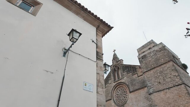 Dynamic POV walk along the historic stone architecture of Carrer de la Rectoria, revealing the grand Sant Jaume Church in Alc&uacute;dia, Mallorca.