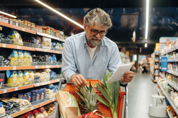 Reading a shopping list. A senior man is buying food in the grocery store