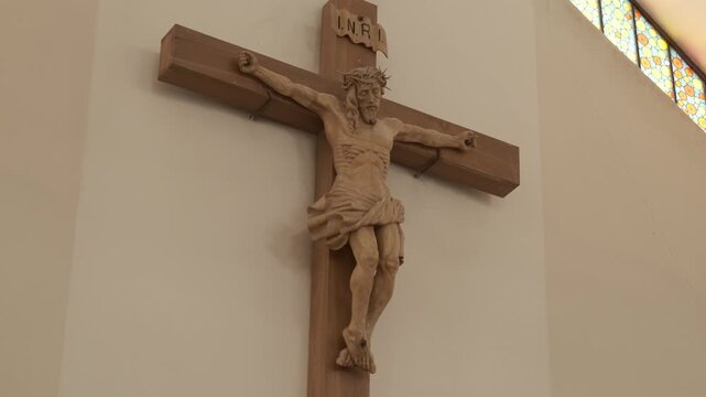 Hand-carved wooden crucifix depicting Jesus Christ on a church wall. Static shot.