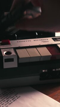 Close up vertical of hand loading cassette tape into analog recorder. Moody lighting. Ideal for crime style, retro music production, interview themes, or technology nostalgia