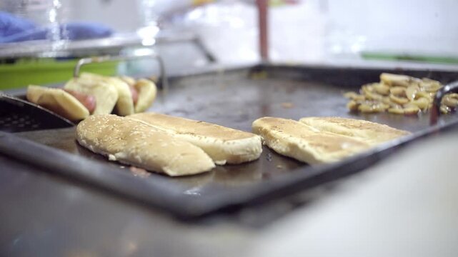 Close up subtle handheld shot of bread slices being toasted on a flat top grill during sandwich preparation.