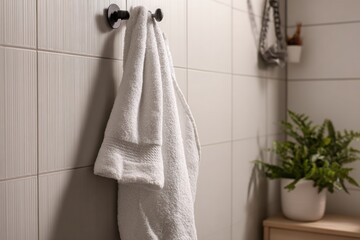 Close up of soft white towel hanging on metal holder against gray textured bathroom wall, showcasing clean modern home interior.