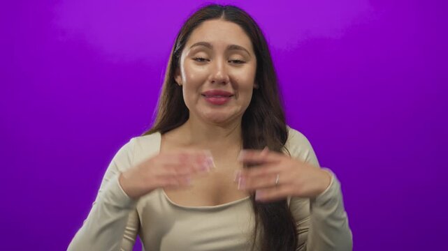 Young hispanic woman shrugs shoulders and holds open hands in purple studio in a questioning gesture; uncertainty.