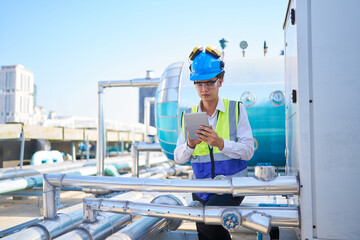 Technician working on tablet and checking pipeline valves or water tank area at urban industrial site