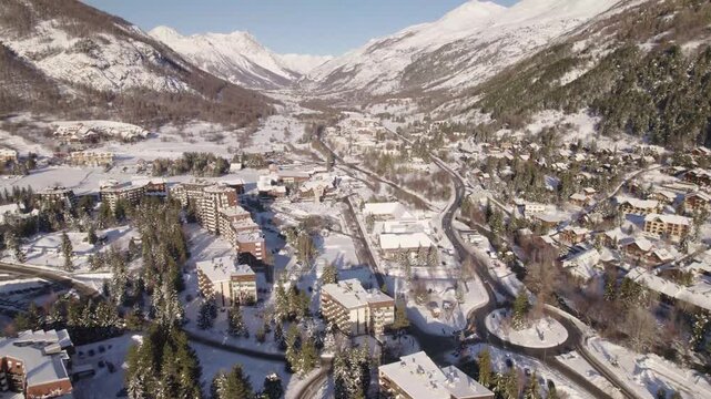 Aerial winter view of La Salle-les-Alpes village in the French Alps, with snow-covered rooftops, winding roads and alpine mountains under clear light.