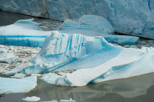 View of jagged icebergs in shades of white and blue float serenely on the water's surface, framed by massive glacial walls, Los Glaciares, Santa Cruz Province, Argentina.