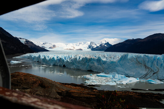 View of the majestic, icy Perito Moreno Glacier calving into the milky waters, framed by rugged mountains and a vibrant sky, El Calafate, Santa Cruz Province, Argentina.