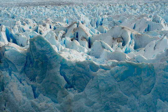 View of glacial ice formations with deep blue crevices under a bright sky, a landscape of stark beauty and cold majesty, Los Glaciares, Santa Cruz Province, Argentina.