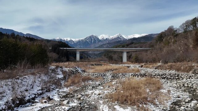 A bridge spans a river with mountains in the background. The bridge is a large structure that spans the width of the river