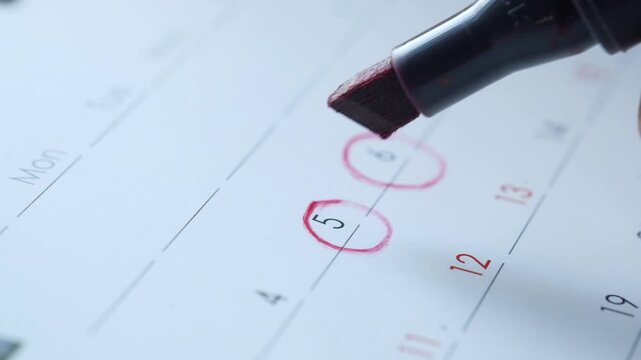 Person marking fifth and sixth dates on calendar with red marker pen closeup shot