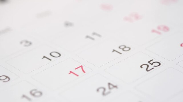 Close up camera panning slowly over a monthly calendar, highlighting the red-colored numbers indicating holidays or weekends in a clean and simple white background