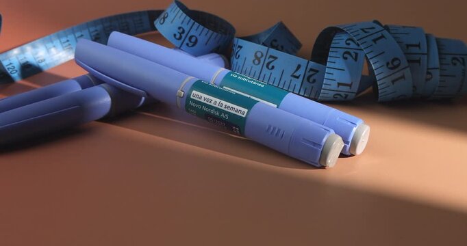 Horizontal pan of blue semaglutide pens and a tape measure for obesity treatment, chronic disease control and medical weight loss.