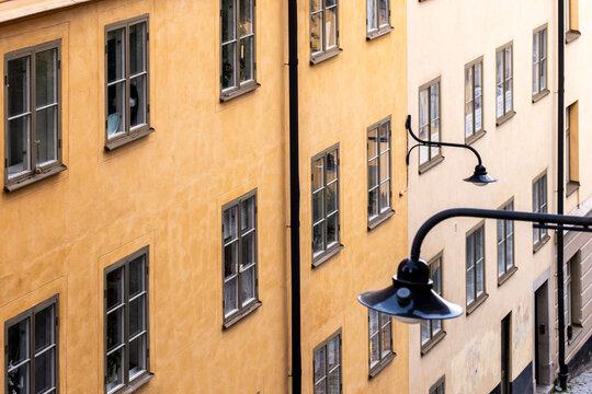Repeating facades show historic architecture in Stockholm Sodermalm Sweden with windows a wall lamp and rich texture on ochre plaster in crisp daylight